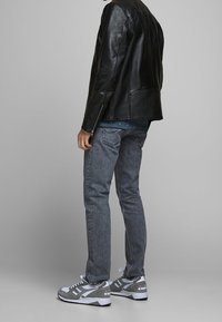 Svart läderjacka, blå skjorta med små mönster, grå jeans och grå sneakers med vita accenter. Stående, sedd från sidan.