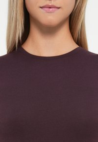 Bordeaux-farbenes, tailliertes Baumwolloberteil mit Rundhalsausschnitt, glatter Textur und schlichten Design, das eine enganliegende Passform um den Kragen zeigt.