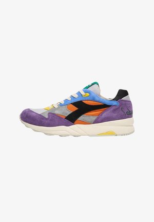 Zapatilla baja de ante morado, con acentos en azul y naranja, logo negro, suela blanca y detalle de lengua verde, sobre un fondo blanco.