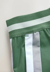 Ceinture de shorts de sport verts et blancs avec une large bande élastique verte comportant une bande blanche horizontale.