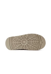 Suela de zapato de goma de color marrón claro con un patrón texturizado de copos de nieve para tracción y agarre, con un elemento de diseño central redondo.