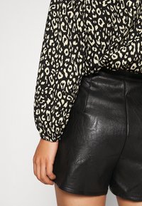 Schwarz-creamfarbener Leopardenprint-Bluse mit langen Ärmeln, kombiniert mit hoch taillierten schwarzen Ledershorts, die eine glatte Textur und eine figurbetonte Passform zeigen.