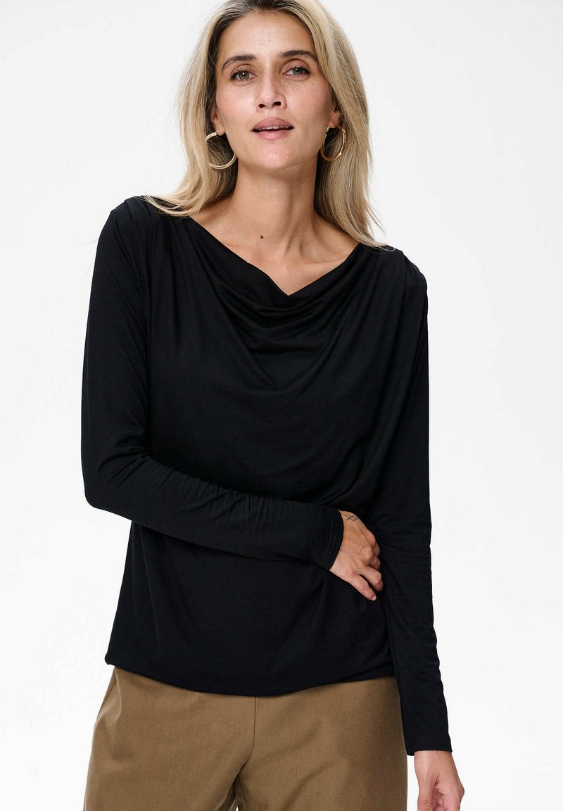Zwart lang mouwtop met een gedrapeerde halslijn en ontspannen pasvorm. Zachte stof en gladde textuur. Gecombineerd met beige high-waisted broek.