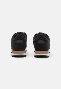 Black sneakers featuring a mix of smooth and textured materials, with a tan outsole and white midsole. Back view showing logo detail.