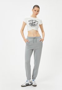 Witte cropped t-shirt met de opdruk "Austin, Texas", gecombineerd met grijze sweatpants met een elastische tailleband en boorden, en zwart-witte sneakers.