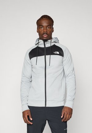 Grå zip-up hættetrøje med sorte accenter og logo. Har snore, en glat tekstur og sidelommer.