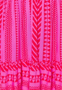 Kirkkaan pinkki kangas, jossa on pystysuoria punaisia geometrisia kuvioita, kuten raitoja, kolmioita, chevronkuvioita ja sahalaitoja, sekä laskostettu sauma alaosassa.