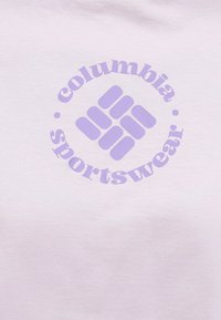 Λογότυπο Columbia Sportswear σε χρώμα λεβάντας με στυλιζαρισμένο διαμάντι και κείμενο σε φόντο από ανοιχτόροζ ύφασμα.