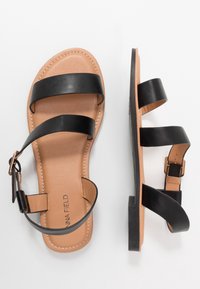 Mustat nahkasandaalit, joissa on kolme leveää remmiä, ruskea sisäpohja ja soljellinen kiinnitys. Tasapohja, jossa ompeludetaili.