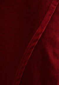 Mélyvörös bársony anyag sima textúrával, átlós varrással és finom fényes felülettel, kiemelve gazdag színét és luxus megjelenését.