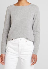 Szary dzianinowy sweter z okrągłym dekoltem, długimi rękawami i prążkowanymi mankietami, zestawiony z białymi jeansami. Miękka faktura i luźny krój.