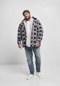 Chaqueta de franela de cuadros en azul marino, rojo y blanco con forro de sherpa, llevada sobre una camisa blanca y combinada con jeans desgastados y zapatillas blancas.