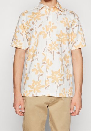 Biała koszula na krótki rękaw z beżowym kwiatowym wzorem, noszona z khaki spodniami, widok z przodu na tułów i ramiona.