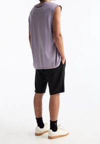 Haut lavande sans manches, shorts noirs avec ourlet effiloché, baskets blanches avec semelle en gomme, vue de dos, mains dans les poches.