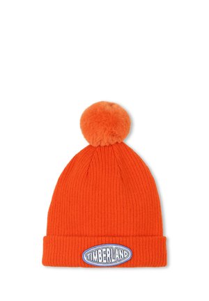 Bonnet en tricot côtelé orange avec un pompon en fausse fourrure sur le dessus et un patch ovale Timberland blanc et bleu à l'avant.