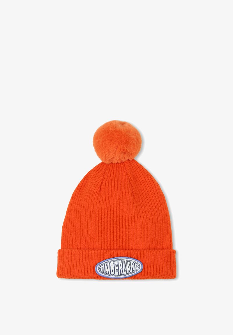 Berretto a costine arancione con un pompon in pelliccia sintetica in cima e una patch ovale bianca e blu con il logo Timberland sul davanti.