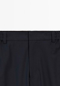 Zwarte broek met elastische tailleband, riemlussen en een ritssluiting aan de voorkant, getoond van de taille naar beneden tegen een witte achtergrond.
