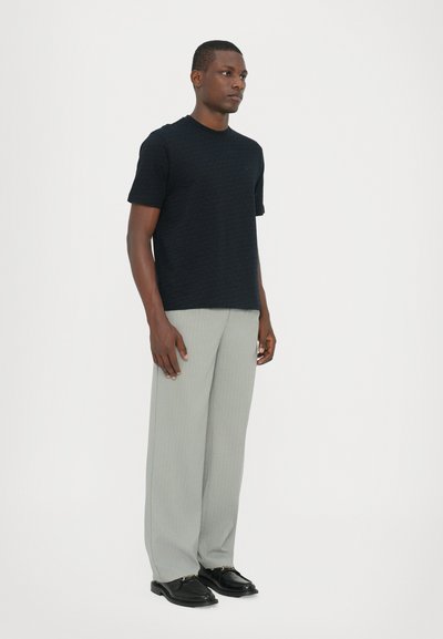 T-shirt noir à manches courtes avec un motif texturé, associé à un pantalon large à rayures fines gris clair et des chaussures noires.