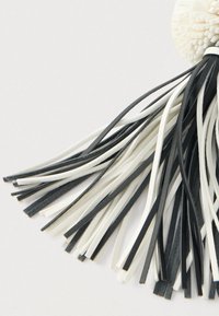 Črno-bele usnjene trakove z resicami so pritrjene na teksturirano belo okroglo podlago na enostavni podlagi.