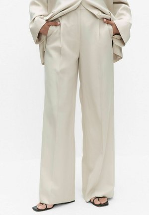 Beige bukser med vide ben og sidelommer, båret med matchende top og sorte sandaler med firkantet tå og tåremme.
