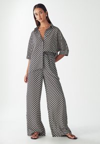 Černo-bílý vzorovaný overal s volným střihem, límečkem, krátkými rukávy a širokými nohavicemi. Hladká struktura látky.