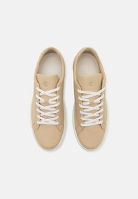 Sneakers in pelle beige con lacci bianchi, punta rotonda e superficie texturizzata. Design minimal con suola in gomma flessibile.