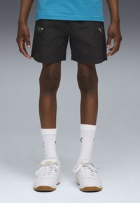 Zwarte shorts van lichtgewicht stof, met een geborduurd ontwerp. Gecombineerd met witte sokken en witte sportschoenen met accenten.