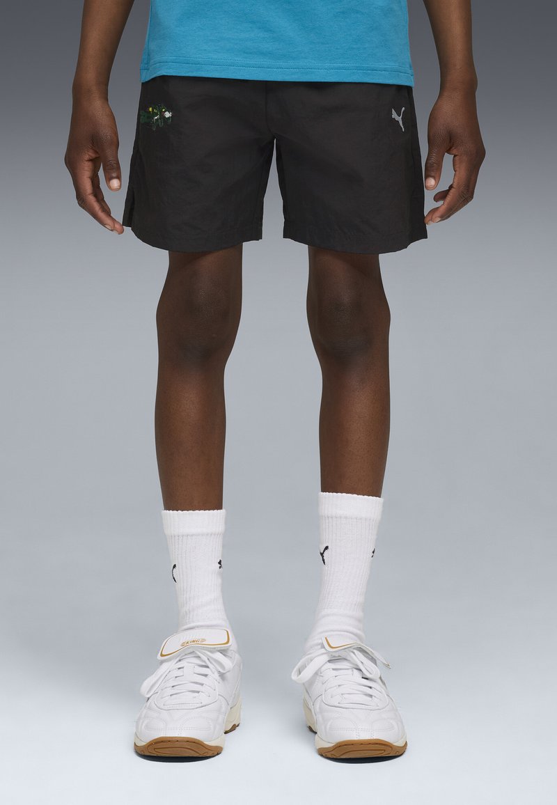 Zwarte shorts van lichtgewicht stof, met een geborduurd ontwerp. Gecombineerd met witte sokken en witte sportschoenen met accenten.