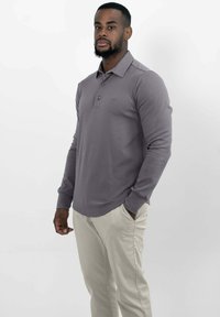 Langarm polo shirt in gedempt grijs, met een knoopsluiting bij de kraag en een subtiele logo, gecombineerd met lichte beige broeken. Glad textuur van de stof.