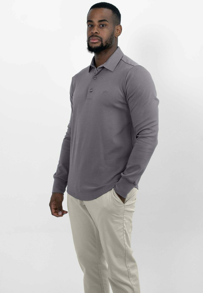 Langarm polo shirt in gedempt grijs, met een knoopsluiting bij de kraag en een subtiele logo, gecombineerd met lichte beige broeken. Glad textuur van de stof.
