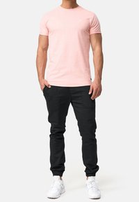 Hellrosa T-Shirt mit kurzen Ärmeln und Rundhalsausschnitt, kombiniert mit schwarzen Jogginghosen mit Seitentaschen und Bündchen, ergänzt durch weiße Sneaker.