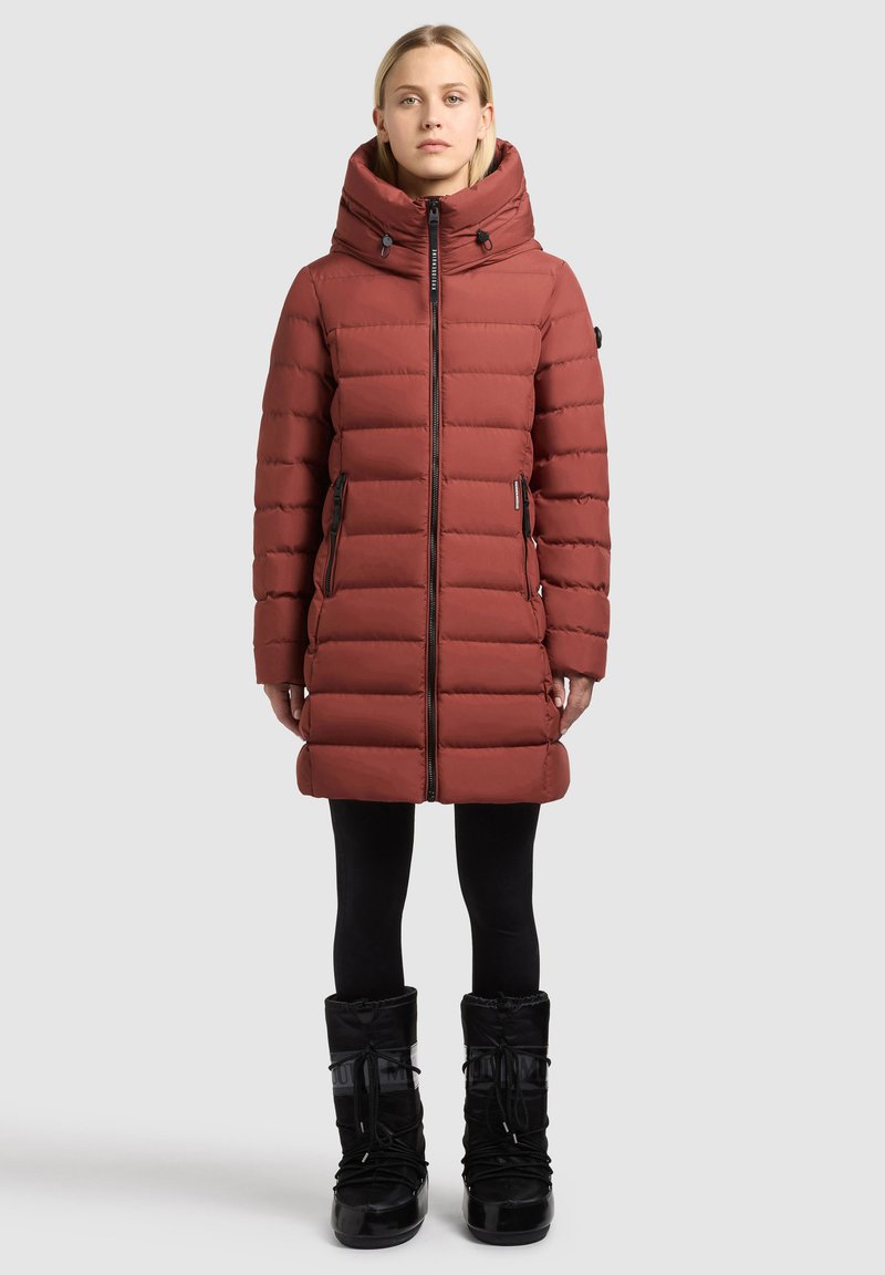 Manteau matelassé rouge avec un col montant, des manches longues et une fermeture éclair à l'avant. Comprend deux poches latérales, un tissu texturé et une coupe élégante. Bottes de neige noires.