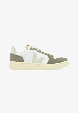 Zapatilla deportiva baja con suela de color blanco roto, cuero blanco y paneles de ante oliva, logotipo "V" beige y cordones blancos, vista desde el lado exterior.
