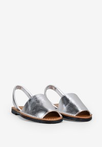 Zapatos slingback de cuero plateado con punta abierta, suela negra plana y diseño sencillo. Textura suave con acentos de hardware mínimos.