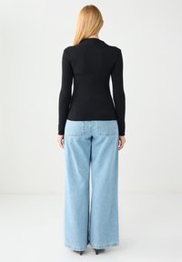 Czarny, dopasowany top z długim rękawem w połączeniu z szerokimi, jasnoniebieskimi jeansami. Top jest obcisły, natomiast jeansy mają luźny krój i widoczne kieszenie.