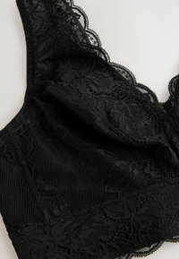 Schwarzer Spitzen-Bralette mit floralem Muster, ausgestattet mit strukturiertem Netz und gewelltem Spitzenrand entlang der Kanten. Weiches und ungepolstertes Design.