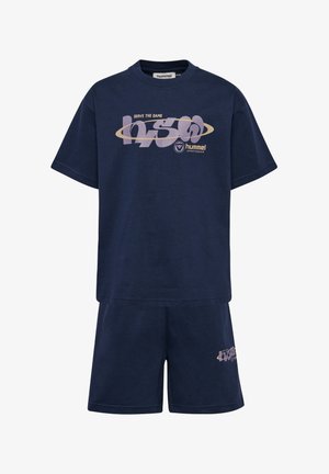 Dwoje dzieci ubranych w pasujące granatowe stroje sportowe z jasnofioletowymi logo, białe skarpetki i jasnoniebieskie trampki, stojących na jednolitym tle.