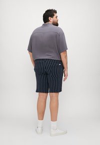 Kortermet grå skjorte med krage, sammen med marineblå stripete shorts. Hvit sneakers og ribbete hvite sokker fullfører antrekket.