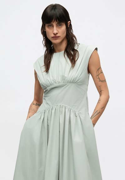 Svetlozelené šaty s krátkymi rukávmi a nariaseným pásom. Tkanina je hladká a splývavá, so stranovými vreckami a rozšírenou sukňou.