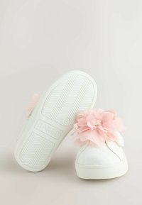 Valkoiset kangaskengät, joissa on teksturoitu pinta, vaaleanpunainen synteettinen kukka koristeena ja kumipohja, jossa on kalanruotokuvio.