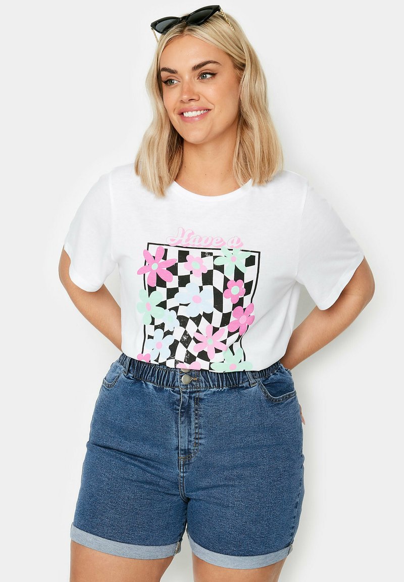Camiseta blanca con un gráfico floral colorido y un diseño a cuadros negro, combinada con pantalones cortos de mezclilla azules con una cintura elástica.