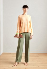 Haut à manches longues orange à fleurs associé à un pantalon large taille haute vert olive. Tient une pochette triangulaire marron avec un accent vert.