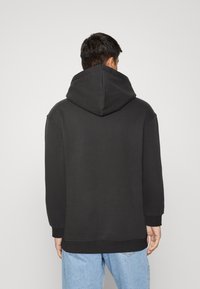 Felpa nera con cappuccio, dal taglio morbido, polsini e orlo a costine. Il tessuto sembra morbido e con una superficie liscia, mostrata dal retro.