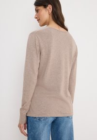 Pull beige à manches longues avec une texture douce, encolure arrondie et manches ajustées. Associé à un jean en denim bleu clair.
