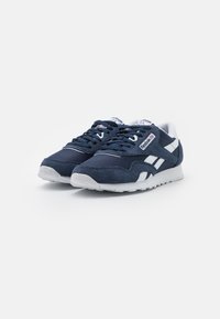 Navy blue sneakers with suede and mesh materials, featuring white accents and a textured rubber sole. Laced design with branding on the tongue.
