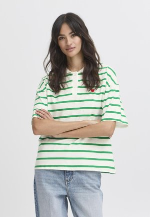 Groen en wit gestreepte polo met korte mouwen en een knoopsluiting bij de kraag, met een klein rood hartlogo op de linkerborst. Draagt met blauwe jeans.