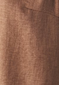 Brauner Stoff mit feiner diagonaler Webstruktur und einer subtilen Taschennahtdetail auf der oberen rechten Seite.