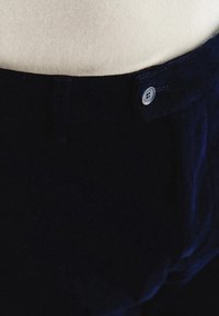 Granatowe welurowe spodnie o gładkiej fakturze, z zapięciem na jeden guzik i klasycznym kroju, z widocznym detalem pasa.