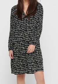 Vestido negro con un patrón de escritura a mano. Mangas largas y diseño de escote en V. Fabricado en una tela ligera con un ajuste relajado.