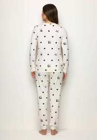 Set di pigiami bianco con pois neri e stampe di panda. Include una maglietta a maniche lunghe e pantaloni abbinati con caviglia a costina. Tessuto morbido.
